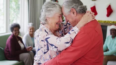 Happy-caucasian-senior-couple-dancing-together-with-friends-in-background-at-christmas-time