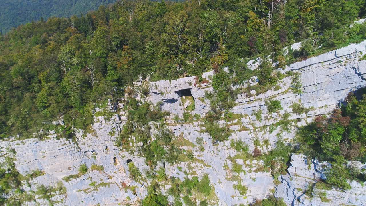 Aerial towards massive cliff face and green trees forest in Kostel