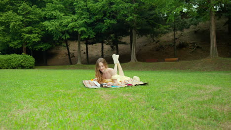 우크라이나 여성 이 공원 에서 피크닉 매트 에 배 에 누워 책을 읽고 있다