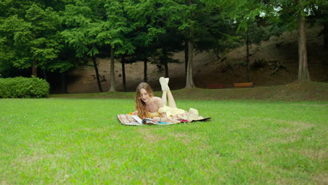 ukrainian woman reading book while lying on her stomach on picnic mat in the park