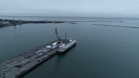 loading shipping containers on a cargo ship on a dark sea - aerial parallax