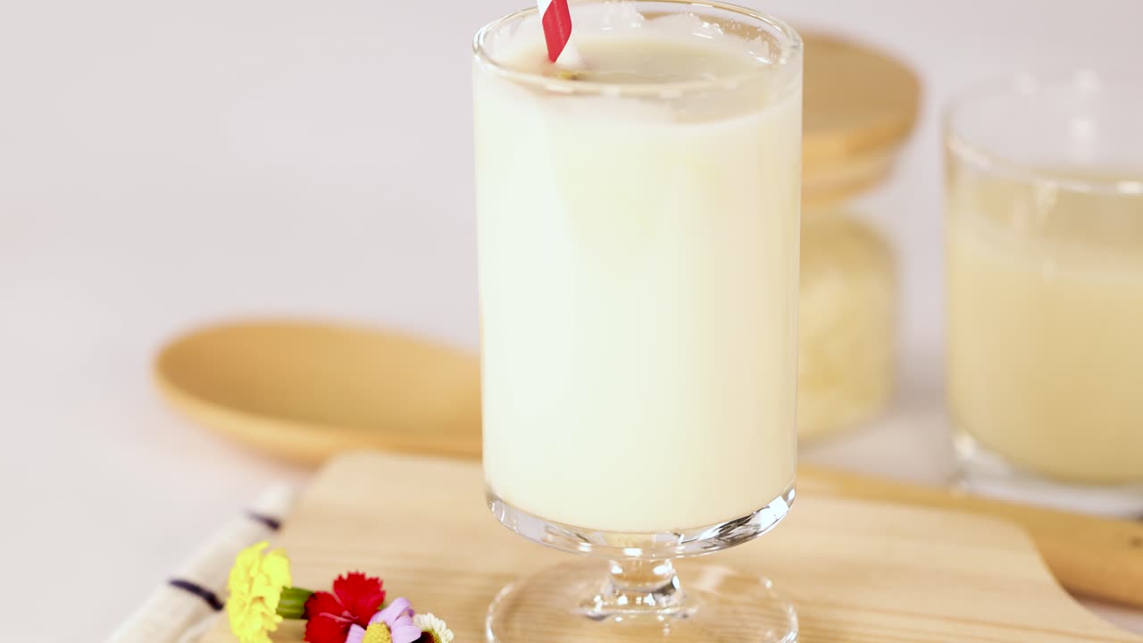 Hand stirs banana milkshake in glass, bright lighting, close-up, smooth camera movement, minimal background