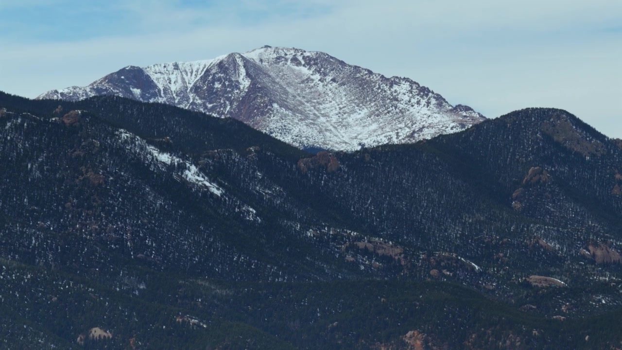 Lumipeitteinen Pike Peak (14er), Colorado Springs, Colorado. Ilmakuva dronella talvisena kevätaamuna, sininen taivas ja pilviä. Coloradon Denverin eteläpuolella sijaitseva Cheyenne-vuoren Front Range Kalliovuorten maisema.