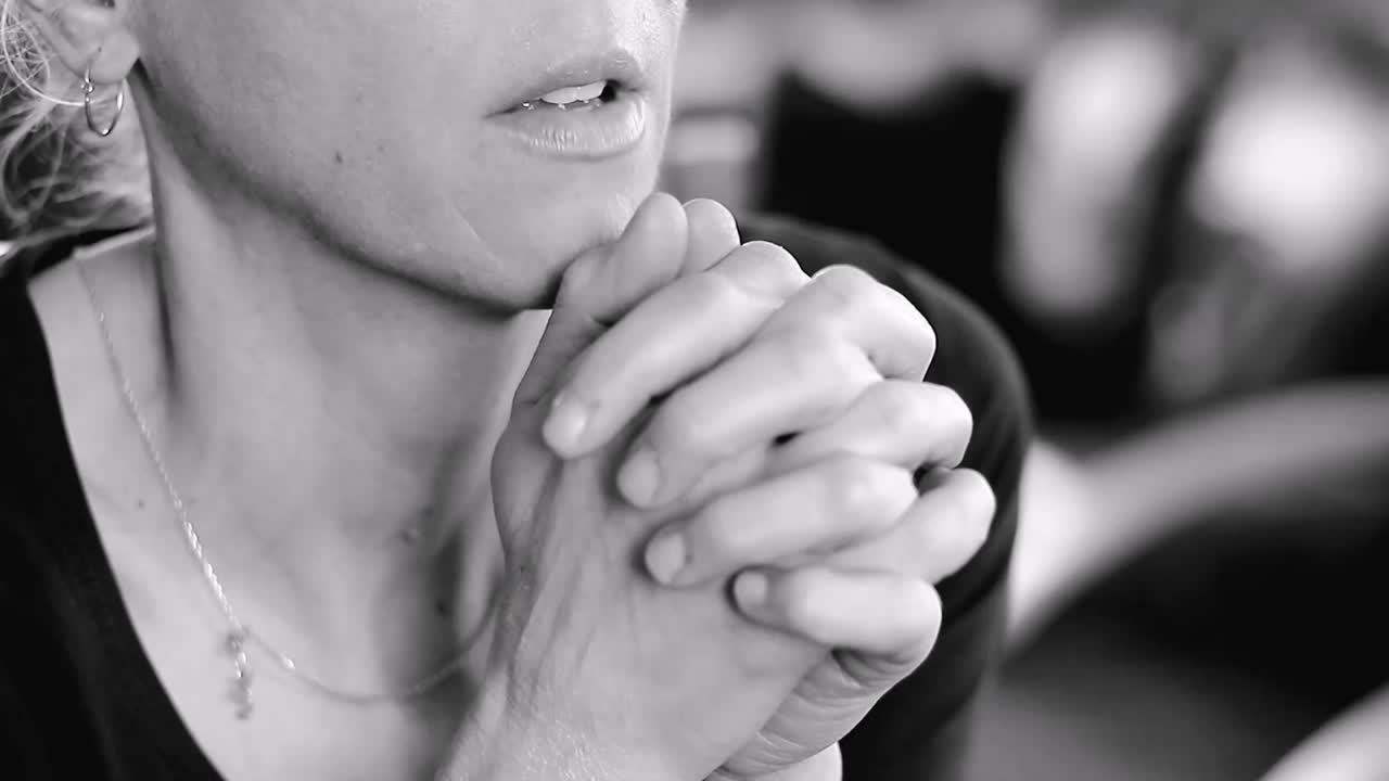 사람들과 회색 배경에 그녀의 얼굴에 손을 대고 기도하는 여자 스톡 비디오