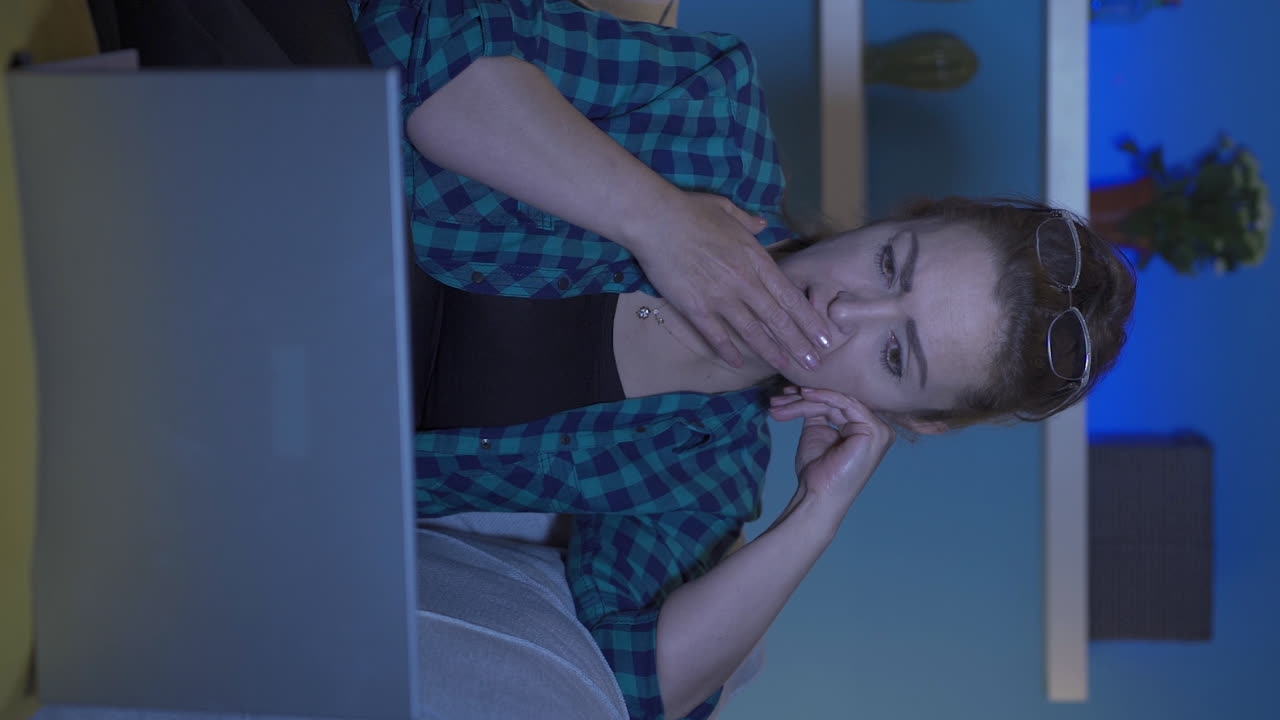 video vertical de una mujer viendo una película en una computadora portátil por la noche en casa.
