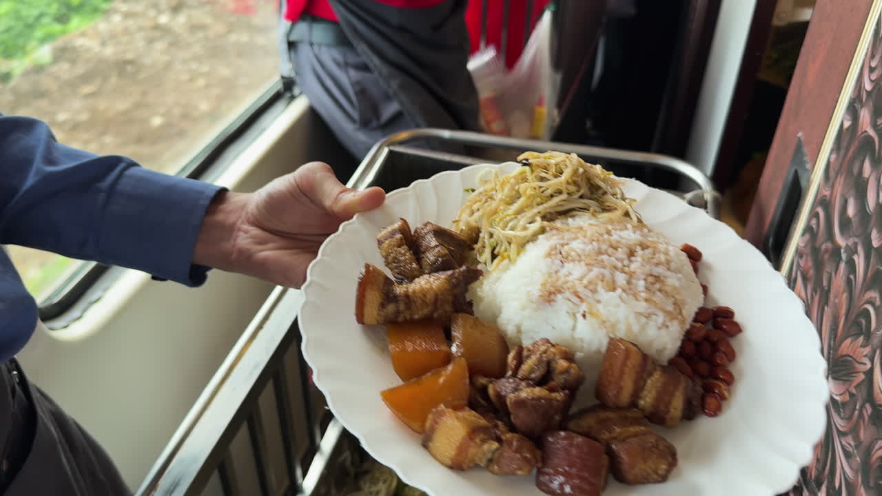Pasto in treno servito dal personale di bordo accanto a un finestrino sulla tratta da Hanoi a Hoi An, con riso, noodles, maiale brasato e fagioli in un momento autentico di cibo da viaggio