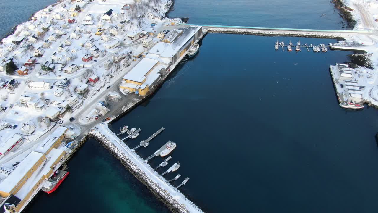 Drone view on the Tromso mountains in winter full of snow showing Husoy a small town on an island surrounded by the sea and its small port with flying seagulls
