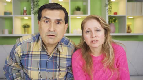 funny mature husband and wife at home looking at camera with great amazement.