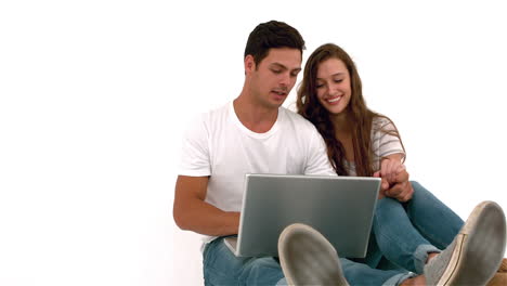 una pareja feliz sentada en el suelo usando una computadora portátil