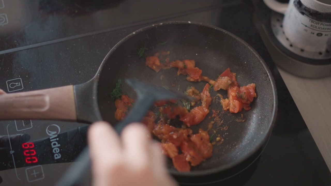 Fresh vegetables being cooked by home chef. Morning kitchen scene with bubbling tomato and fragrant herbs. Home chef actively stirs sizzling tomato pieces infused with aromatic herbs in kitchen