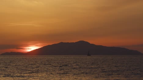 close-up of ischia island from anacapri with a silhouetted sailboat on the ocean at sunset