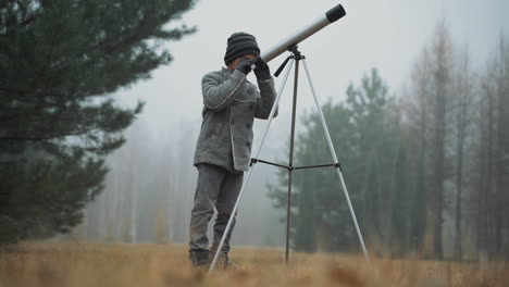 un ragazzino che guarda attraverso un telescopio nella foresta. ragazzo interessato all'astronomia e alla scienza.