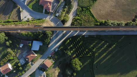 Bird's-eye-view-of-Old-arch-railway-bridge-surrounded-by-crop-fields-at-dusk---Ponte-Seca,-Durrães,-Barcelos