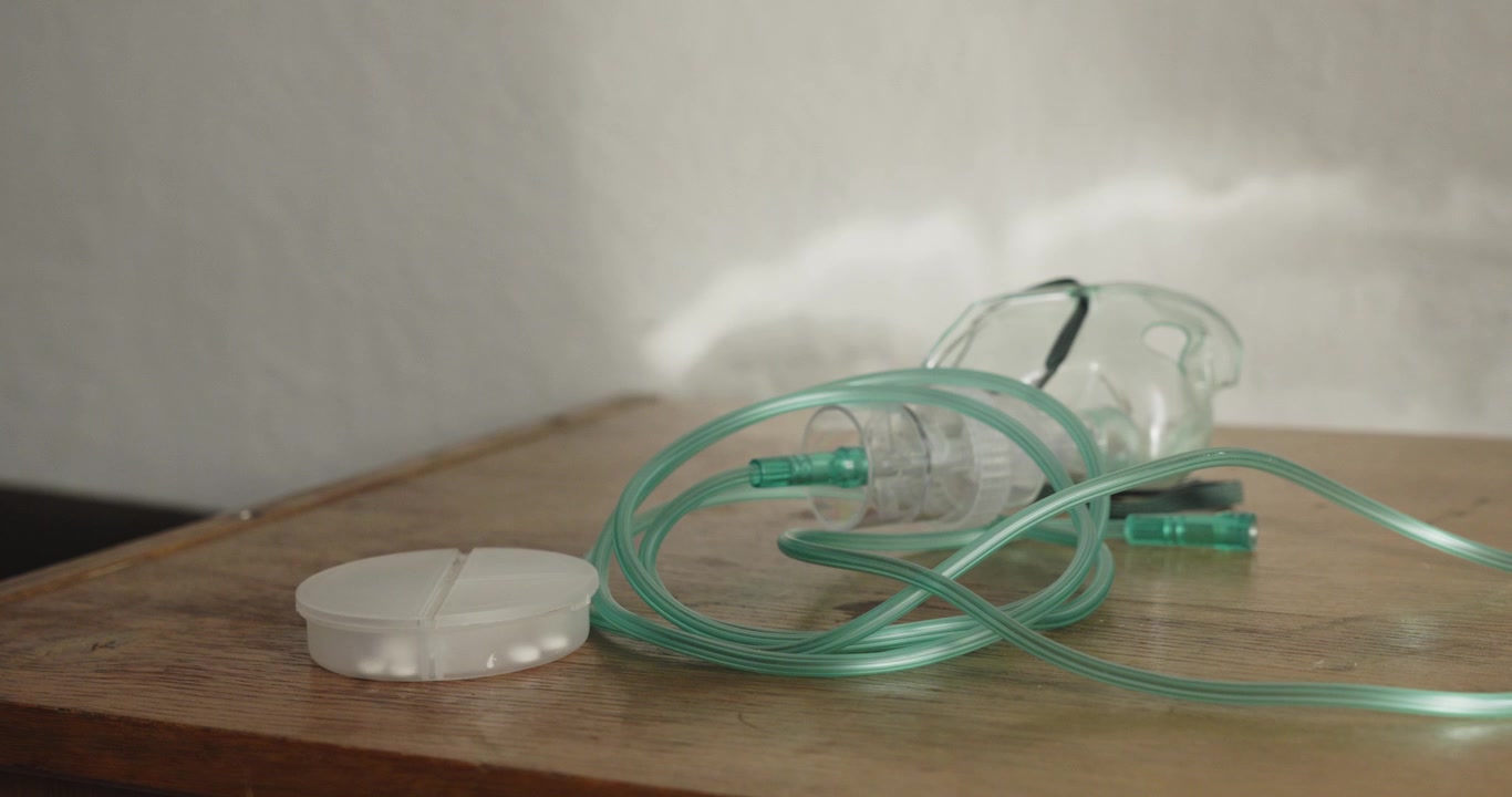 Una mano raccoglie un apparecchio per maschera d'ossigeno da un comodino durante una scena allestita di ossigenoterapia domiciliare e assistenza per malattia