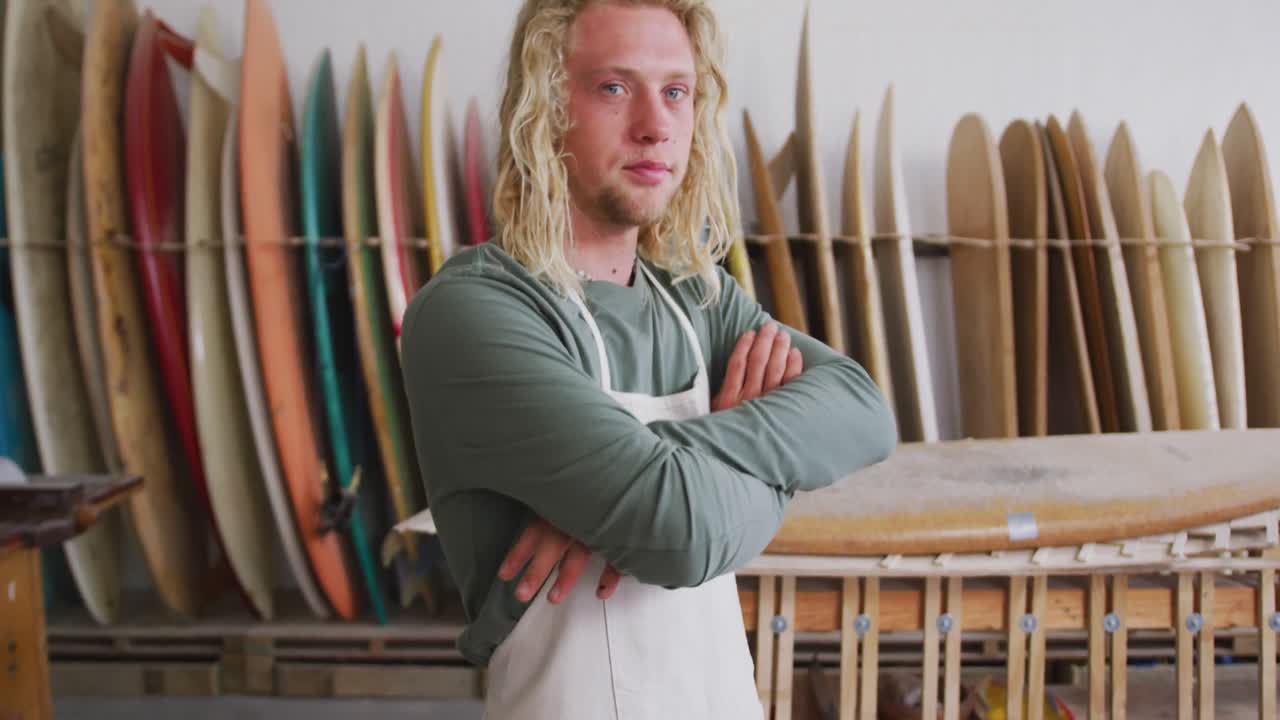 Kaukasisk mandlig surfbrætbygger iført beskyttelsesforklæde med krydsede arme.