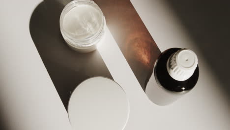 high angle view of glass bottle and cream tubs with copy space on white background
