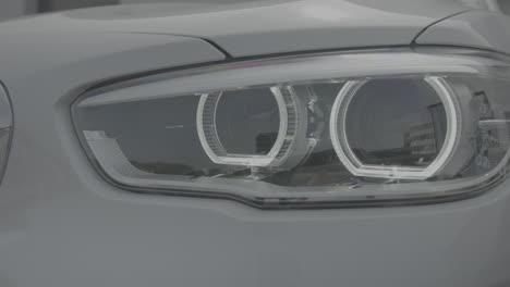 closeup shot of led headlights of a white car lighting up when starting the car log