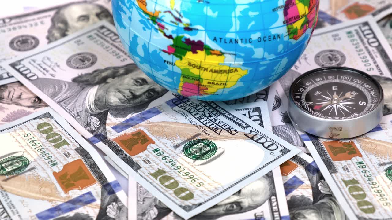 primer plano de la brújula y el globo del planeta tierra sobre un fondo de muchos billetes de 100 dólares en una mesa giratoria. concepto de viajes, turismo, aventuras.