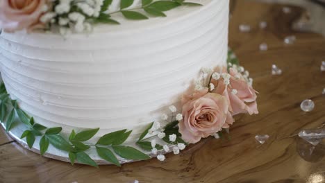 close up of a white wedding cake adorned with pink roses, greenery, and delicate details