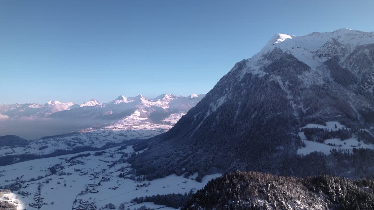 Veduta aerea di un paesaggio montano innevato con boschi in una soleggiata giornata invernale in Svizzera