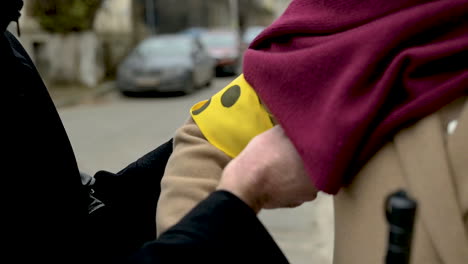 man putting an yellow armband with three black points on a blind woman in the street