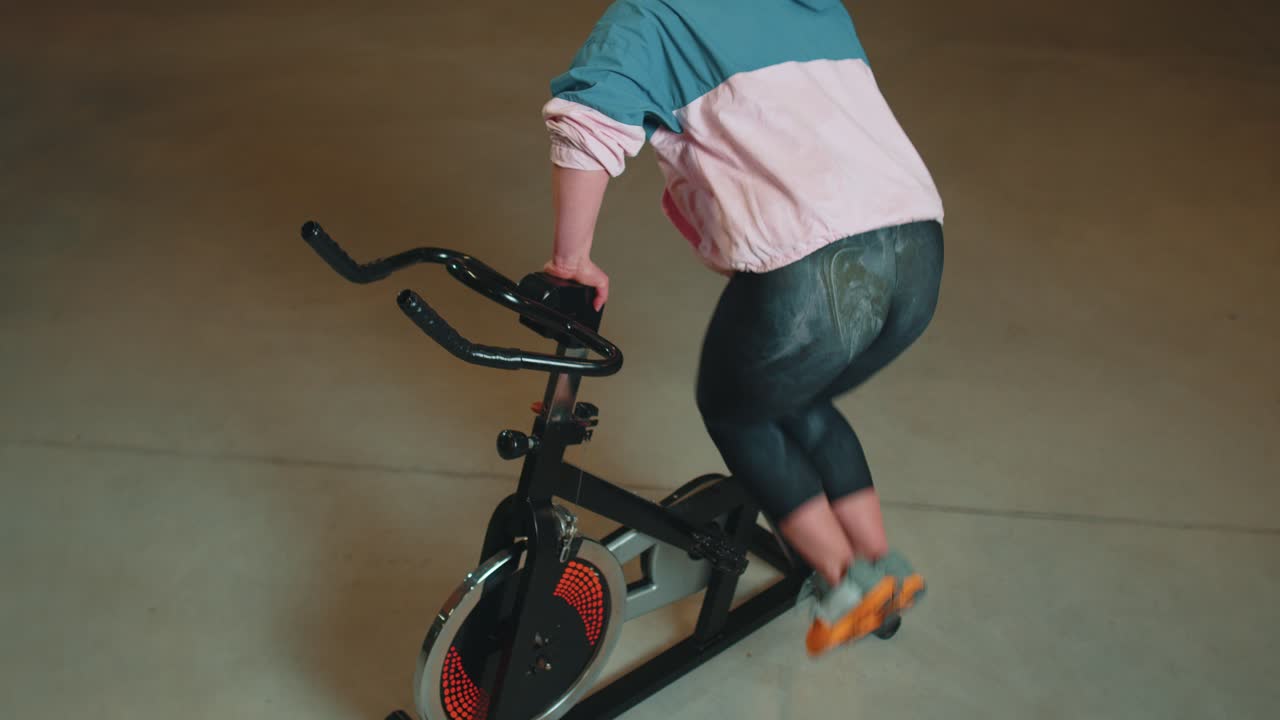 운동하는 소녀는 자전거에서 아크로바틱 트릭을 하고 실내에서 정지 자전거 기계에서 운동을 합니다.