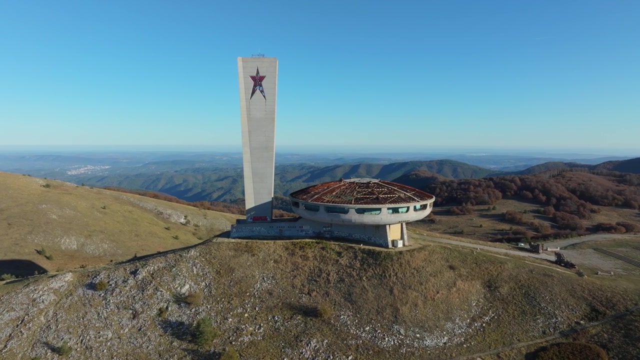 Aerial footage slowly orbiting the Buzludzha monument, an abandoned soviet relic standing on a mountain top in Bulgaria on a sunny day