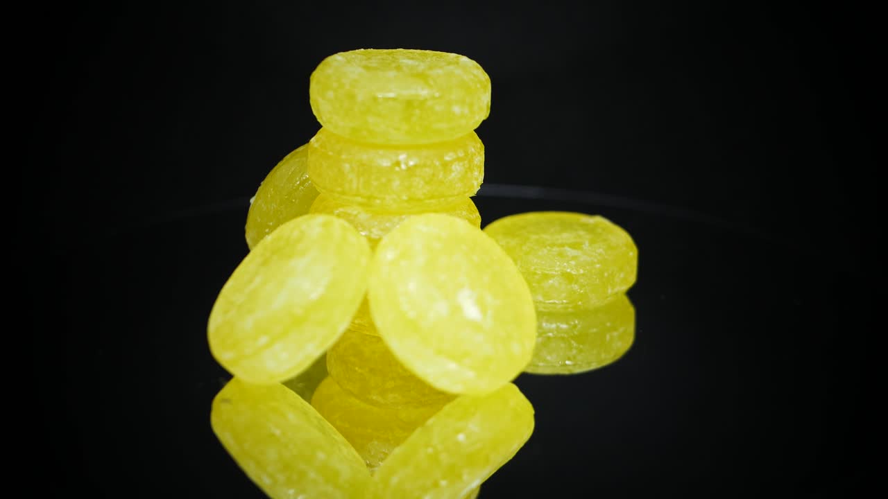 유리 검은색 표면에 반사되어 회전하는 달콤한 레몬 사탕 더미