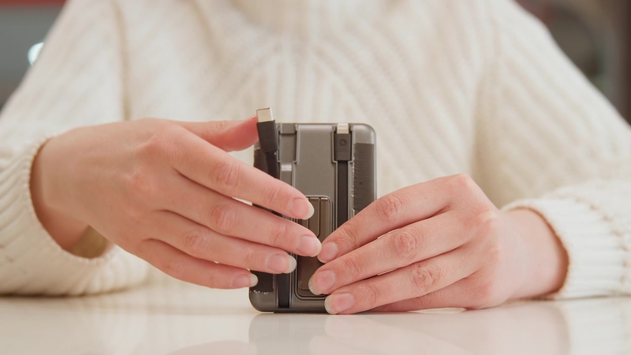 Close-up of both hands carefully reassembling partially disassembled smartphone on tabletop, one hand inserting internal component while other hand steadies device during precise repair work