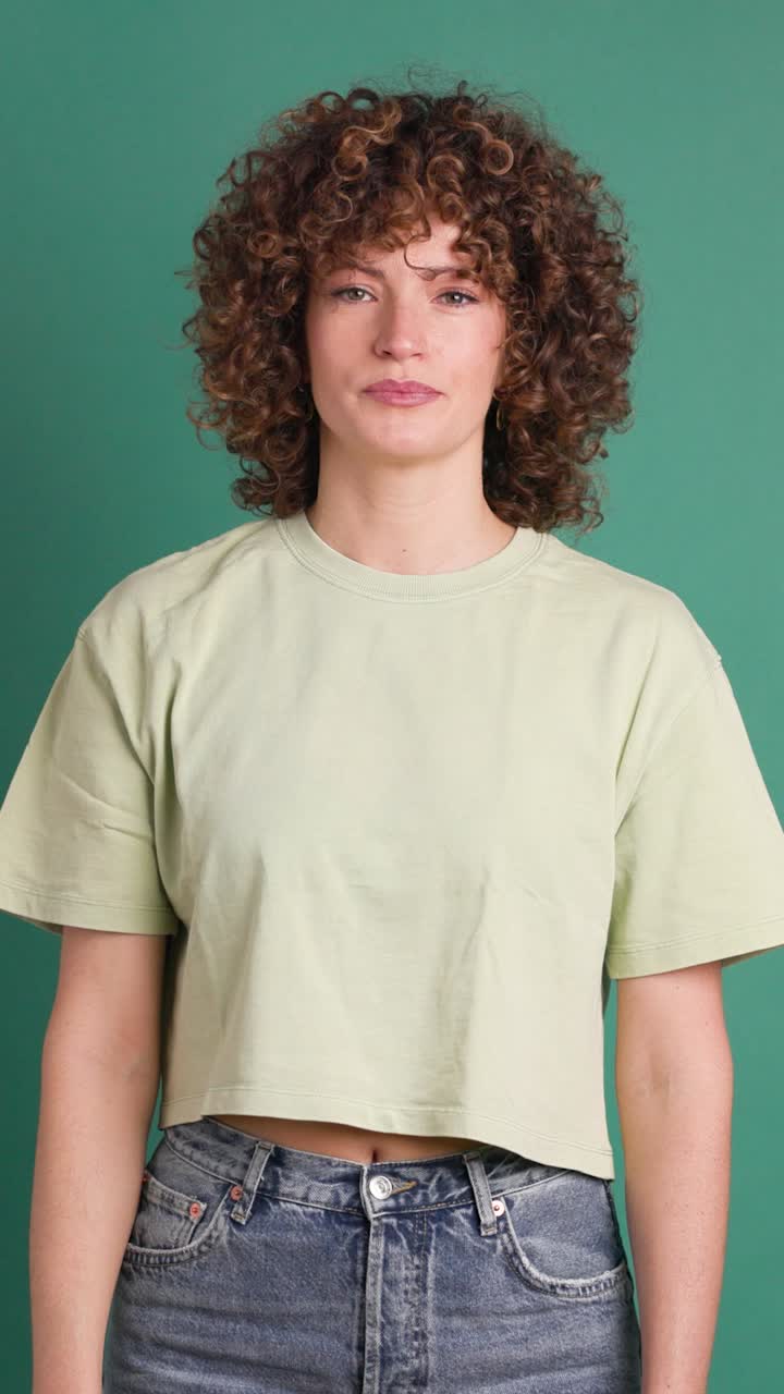 Adult woman with curly hair looking unhappy showing thumbs down gesture. Vertical orientation