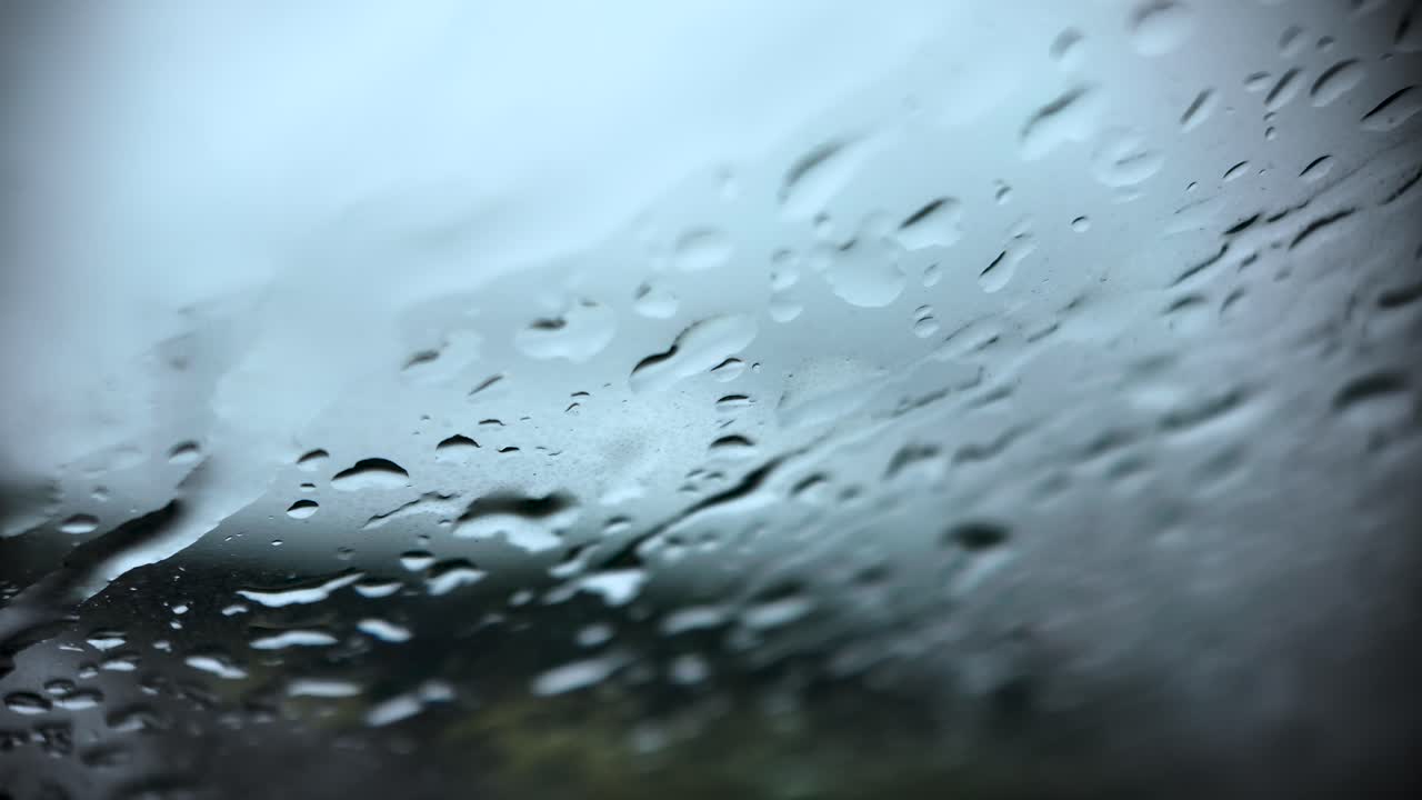 Close up of rain droplets on a windshield, creating a soft blue, blurred view