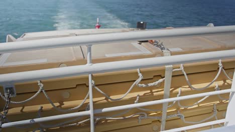 the back of a ferry moving along the sea with the wake and flying flag in background