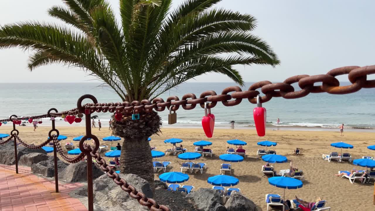 Red love padlocks attached to rusty chain by beach in Lanzarote