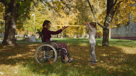 woman with spinal cord injury and girl throw up dry leaves