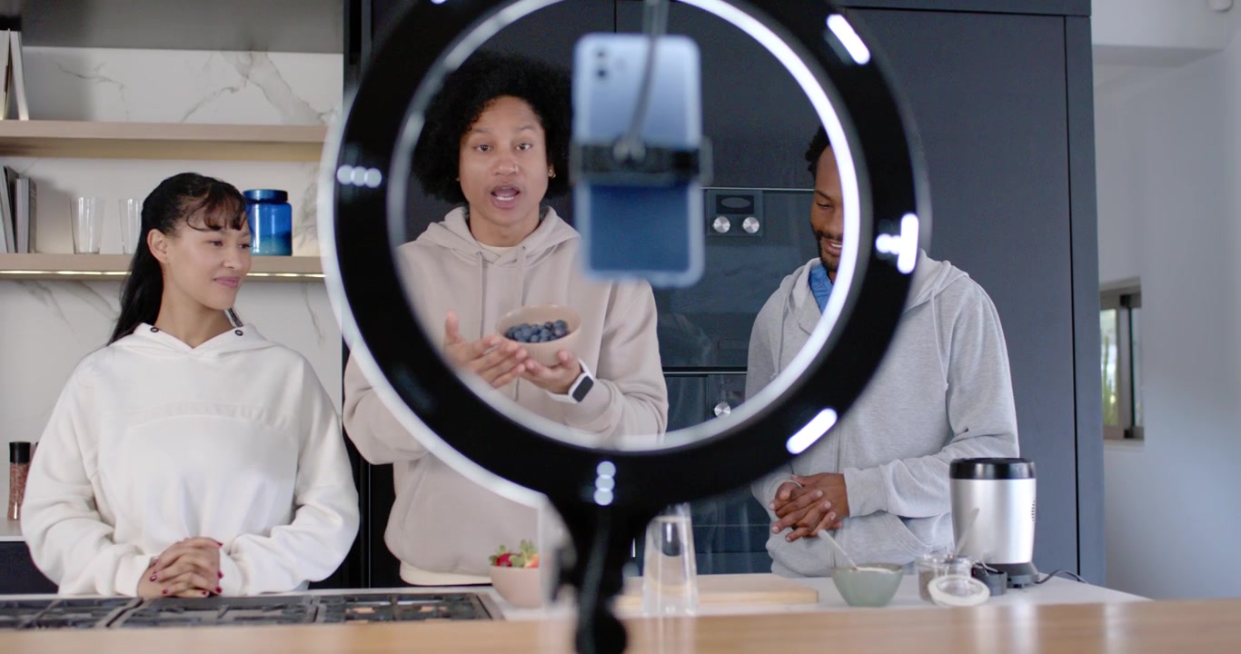 African American trio filming in kitchen with ring light phone, host showing blueberries presenting