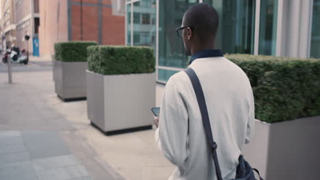 african american businessman walking through city using smart phone