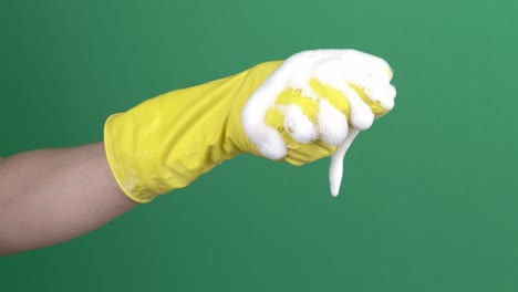 woman hand in yellow protective rubber glove squeezes blue cleaning sponge over green background. 4k video