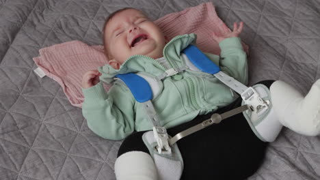 baby girl in pavlik harness to correct hip dysplasia cries while lying on back