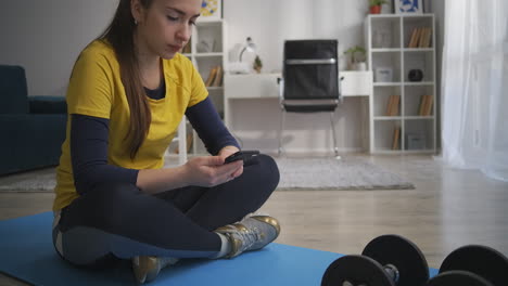 Teenager-Mädchen-Entspannt-Sich-Nach-Dem-Training-Zu-Hause,-Sitzt-Auf-Dem-Boden-Und-Liest-Videos-In-Sozialen-Medien,-Internetsucht-Von-Jugendlichen-Und-Teenagern,-Sportlicher-Lebensstil