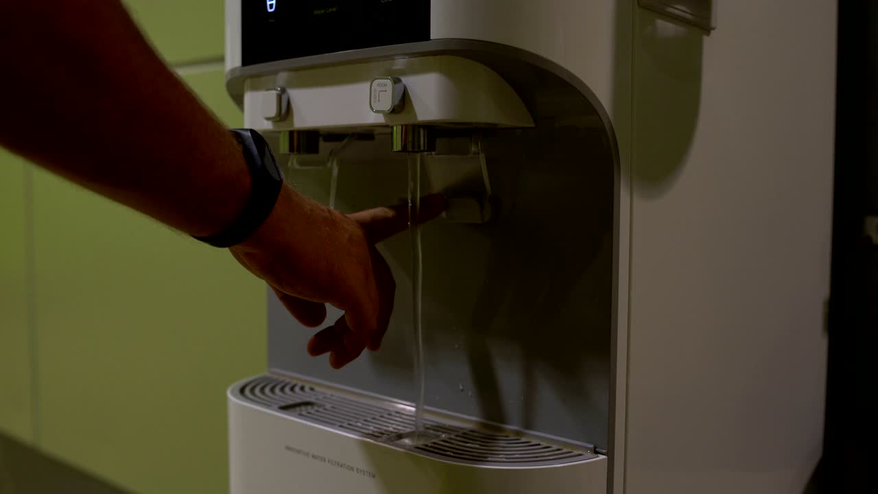 La main appuie sur le bouton du distributeur d'eau et l'eau coule