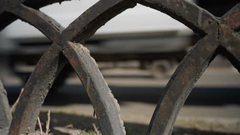 close view of a weathered metal fence with intricate patterns,with cars passing by the road with a blur view of a city building