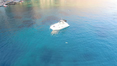 Drone-view-in-Greece-top-view-over-blue-sea-in-Loutro-and-ascend-to-small-white-house-town-and-small-boats-next-to-a-hill-on-a-sunny-day