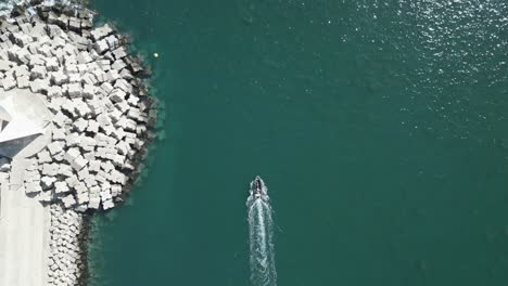 drone top down tracking follows boat with large wake exiting from harbor around breakwater jetty