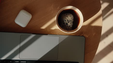 top down shot of hot coffee getting poured from thermos in a mug next to laptop in home office