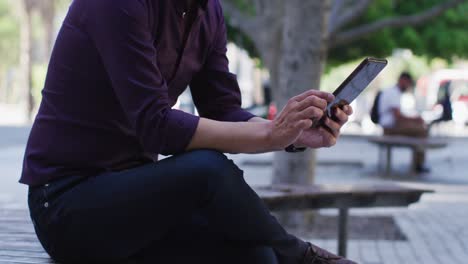 mid section of man using digital tablet while sitting on a bench on the street