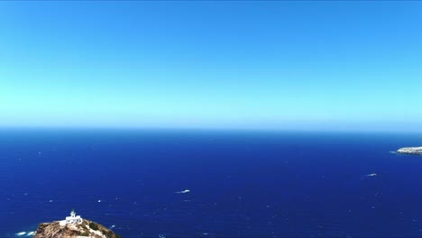 vista aérea de 4k azul del mar y el cielo sobre el faro de akrotiri mientras los barcos compiten en santorini, grecia