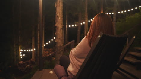 a woman sits on a porch at night, relaxing and enjoying the peaceful atmosphere