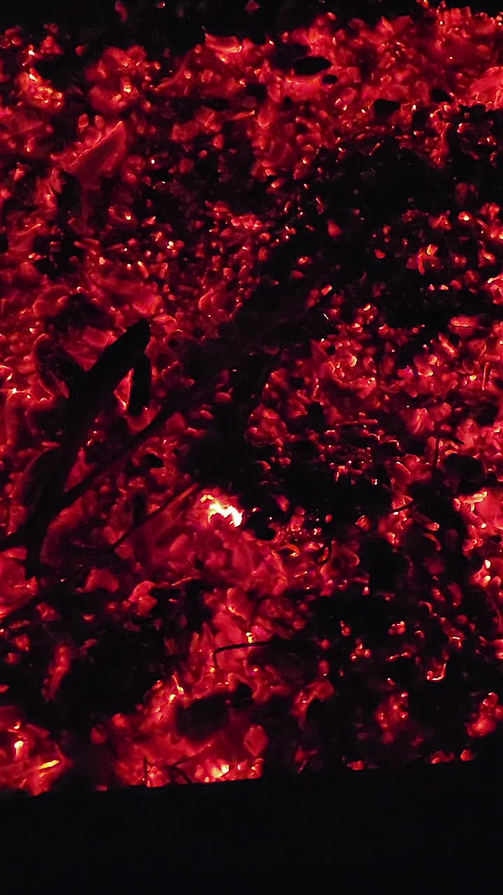 Close-up panning shot of glowing red fire embers and burning coals in a fire pit, creating a dramatic abstract texture of heat, energy, and warmth ideal for themes of camping, power, and survival