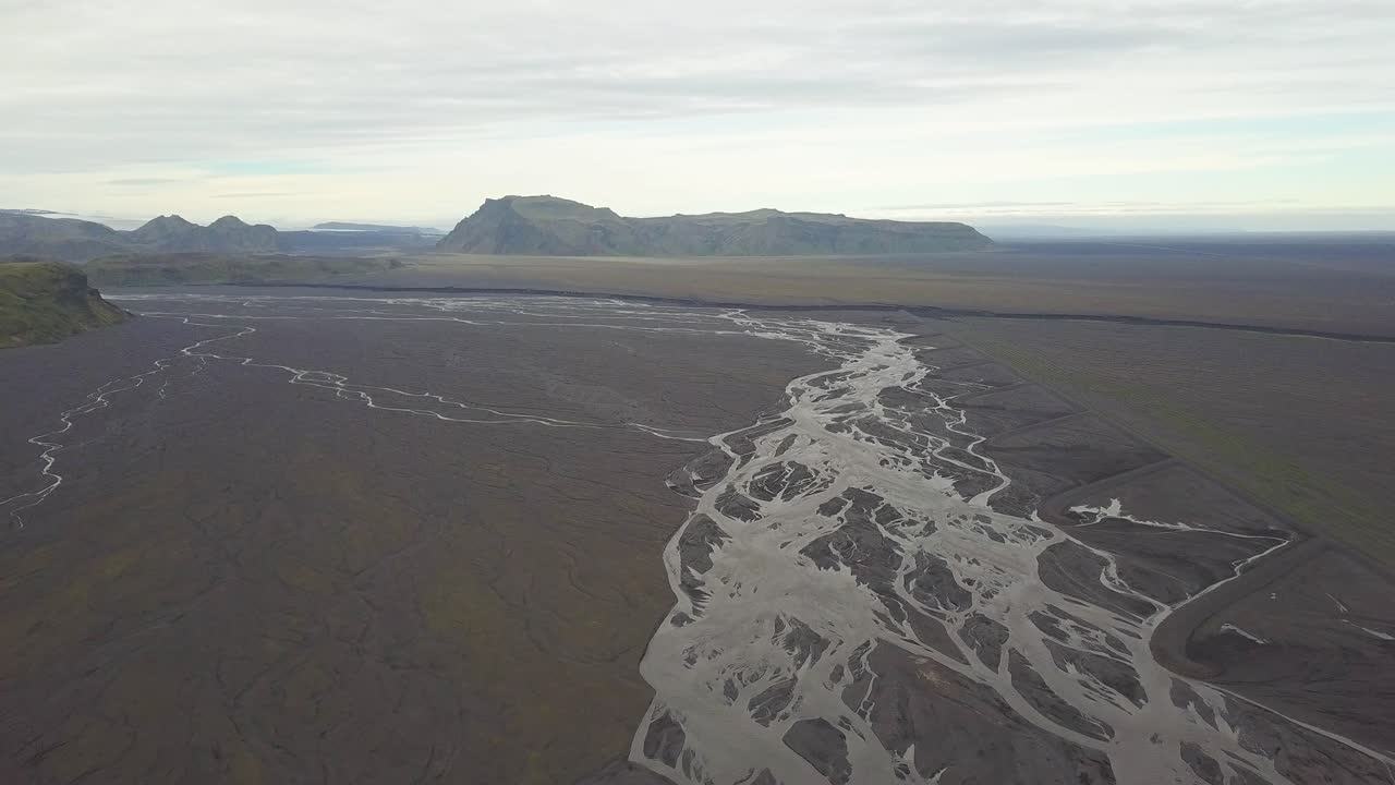 Ripresa aerea in movimento di un corso d'acqua in una zona di fiordi di pianura, con colline verdeggianti sullo sfondo in una giornata nuvolosa, Islanda.