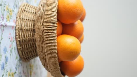 a close-up of a wicker basket filled with fresh oranges on a floral tablecloth